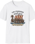 A white short-sleeve crewneck t-shirt featuring a vintage-style graphic of a Viking longship with the text 'LOW STANDARDS HIGH SEAS' and a banner reading 'WE CARRY, WE SAIL, WE GROW, AND WE OVERCOME'.