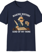 A navy blue short-sleeve t-shirt with a graphic print of a cartoon George Washington holding a newspaper that reads 'I, John Adams' while writing. The text above and below reads 'MAKING HISTORY IS - KIND OF MY THING' in white.